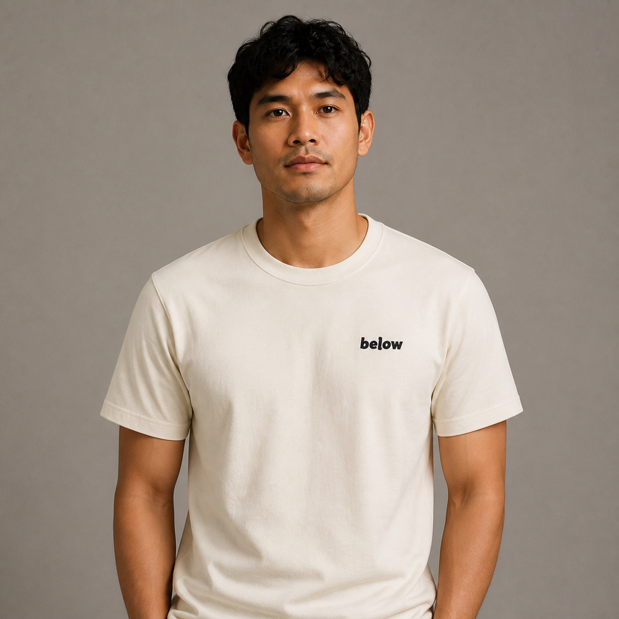 Persona con camiseta crema Below sobre fondo gris cálido