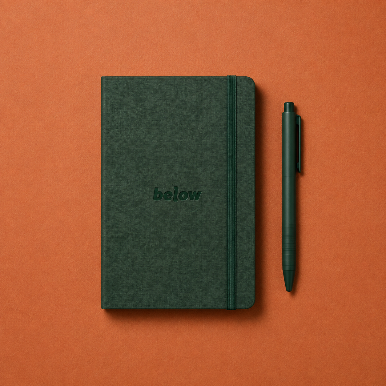 Cuaderno y bolígrafo verdes Below sobre fondo terracota